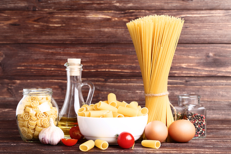 Different pasta with tomatoes, garlic, eggs and oil on brown wooden tableの写真素材