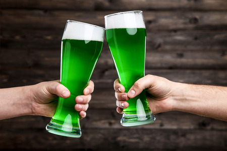 St. Patrick's Day. Glasses of green beer in male hands on wooden backgroundの写真素材