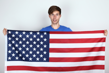 Beautiful young man holding an American flag on grey backgroundの写真素材