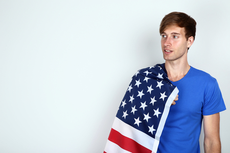 Beautiful young man holding an American flag on grey backgroundの写真素材