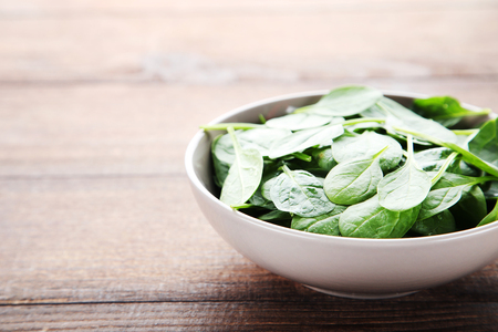 Spinach leafs in bowl on brown wooden tableの写真素材