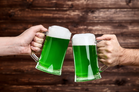 St. Patrick's Day. Glass mugs with green beer in male hands on wooden backgroundの写真素材