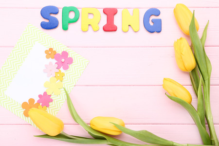 Yellow tulips with greeting card and word Spring on pink wooden table