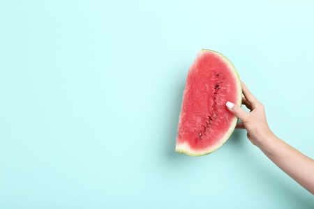 Female hand holding sliced of watermelon on mint background