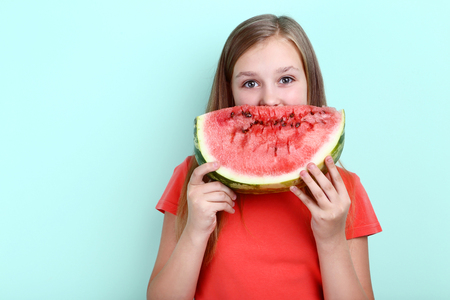 Cute young girl with slice of watermelon on mint backgroundの写真素材