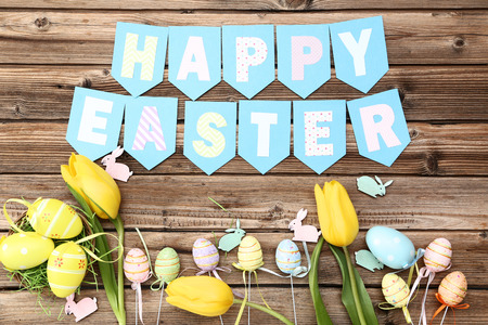 Yellow tulips with eggs, small rabbits and text Happy Easter on wooden tableの写真素材