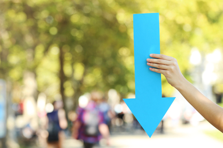 Female hands holding blue paper arrow on the street