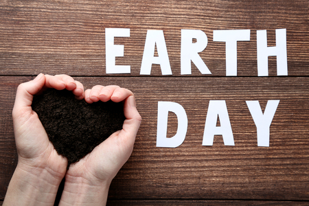 Female hands holding ground with inscription Earth Day on wooden tableの写真素材