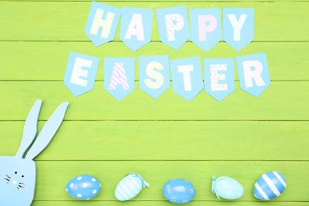 Painted eggs with wooden rabbit and text Happy Easter on green tableの写真素材