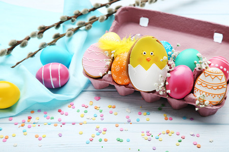Colorful easter eggs in carton box with flowers and gingerbread cookies on wooden table
