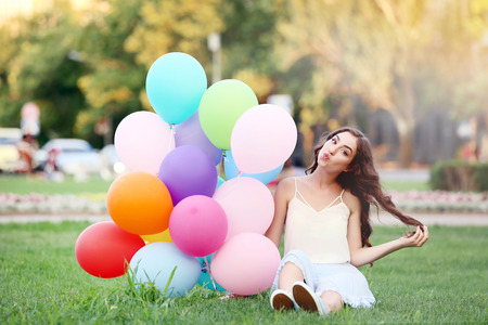Beautiful girl with colored balloons sitting on green grassの写真素材