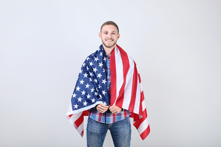 Young man holding an American flag on grey backgroundの写真素材