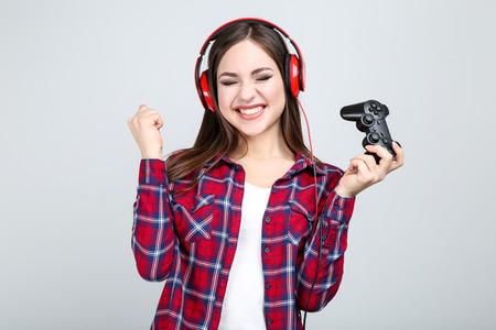 Beautiful girl with joystick and headphones on grey background