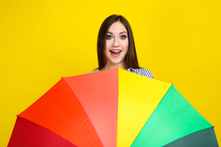 Young girl with colorful umbrella on yellow backgroundの写真素材