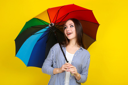 Young girl with colorful umbrella on yellow backgroundの写真素材