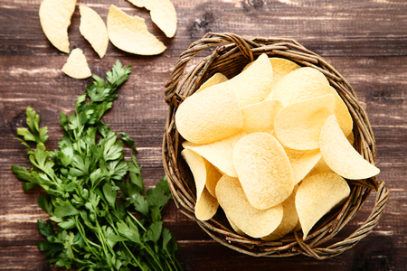 Potato chips in basket with green parsley on wooden tableの写真素材