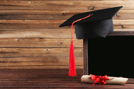 Graduation cap with diploma and blank frame on brown wooden tableの写真素材