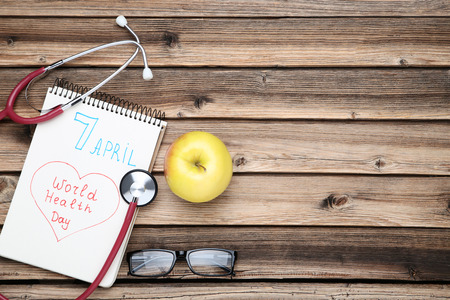 Text World Health Day with stethoscope, glasses and apple fruit on brown wooden tableの写真素材