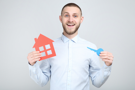 Young man with paper house and key on grey backgroundの写真素材