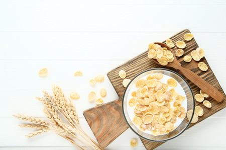 Corn flakes in milk with wheat ears on white wooden table