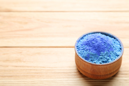 Holi powder in bowl on brown wooden tableの写真素材