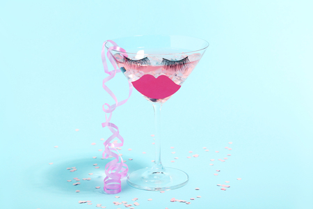 Cocktail in glass with eyelashes, paper lips and ribbon on blue background. Minimalism conceptの写真素材