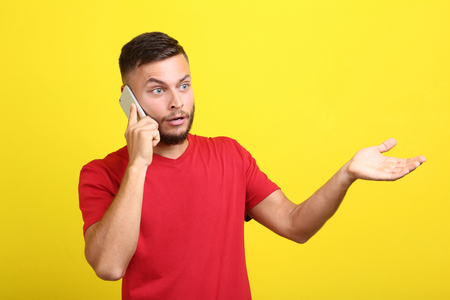 Young man talking on a mobile phone on yellow backgroundの写真素材