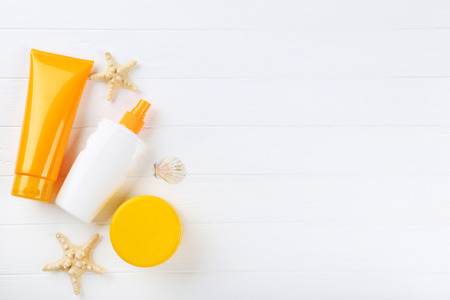 Sunscreen bottles with seashells on white wooden table