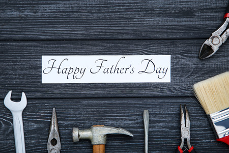 Text Happy Fathers Day with tools on black wooden table