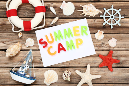 Text Summer camp with seashells, lifebuoy and decorative ship on brown wooden tableの写真素材