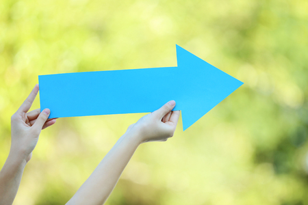 Female hands holding blue paper arrow on the streetの写真素材