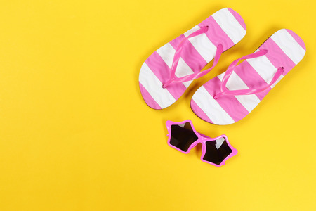 Pair of flip flops with sunglasses on yellow backgroundの写真素材