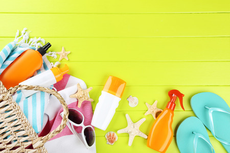 Sunscreen bottles with seashells, towels and flip flops on green wooden table