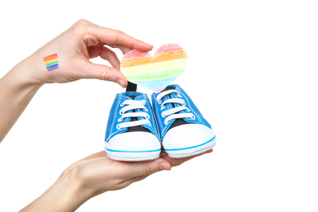 Female hand with drawing rainbow flag, paper heart and baby shoes on white backgroundの写真素材