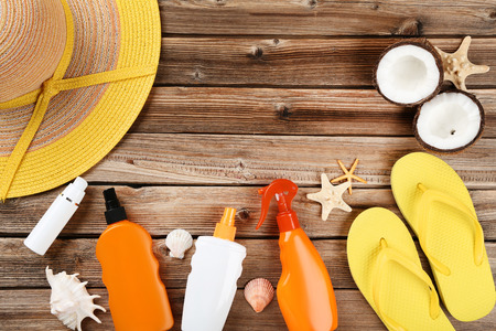 Sunscreen bottles with seashells and flip flops on brown wooden table