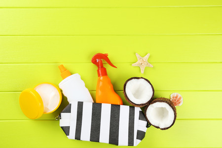 Sunscreen bottles with seashells, coconuts and case on green wooden table