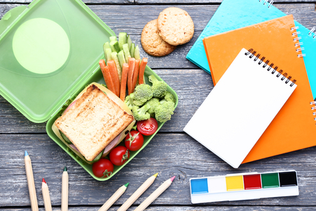 School lunch box with sandwich and notebooks on wooden tableの写真素材