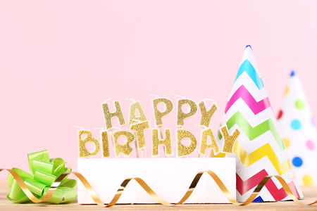 Happy Birthday candles with ribbon and paper cap on pink backgroundの写真素材