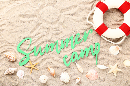 Paper text Summer camp with seashells and lifebuoy on beach sandの写真素材