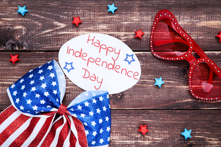 Text Happy Independence Day with sunglasses and american flag in bow on brown wooden tableの写真素材