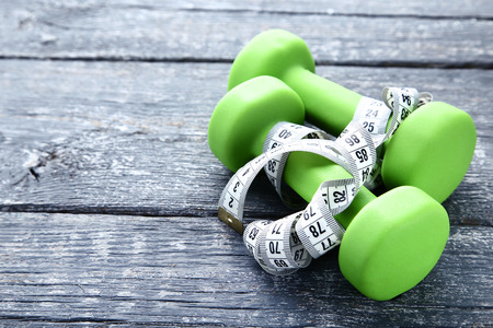 Dumbbells and measuring tape on grey wooden tableの写真素材