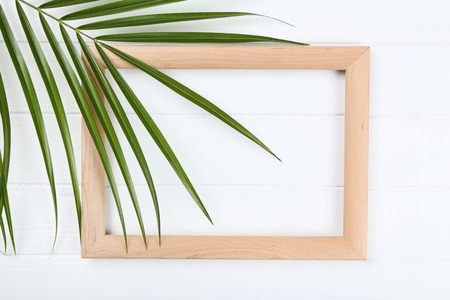 Wooden blank frame with palm leaf on white table
