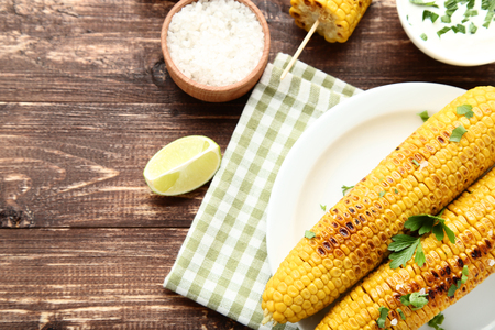 Grilled corn with lime piece, parsley and salt on wooden tableの写真素材