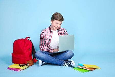 Young boy with laptop and books sitting on blue backgroundの写真素材