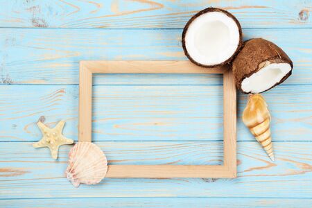 Wooden blank frame with seashells and coconuts on blue tableの写真素材