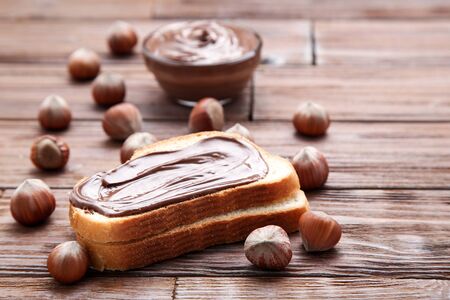 Bread with melted chocolate and hazelnuts on wooden tableの写真素材