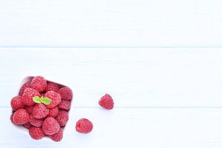 Ripe raspberries with green leafs on white wooden table