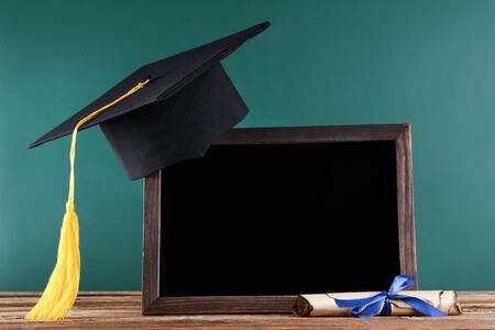 Graduation cap with diploma and blank frame on green board backgroundの写真素材
