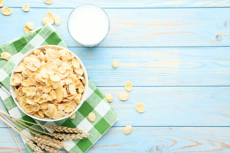 Corn flakes in bowl with wheat ears and glass of milk on wooden table