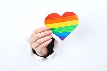 Hand holding paper rainbow heart from white torn paperの写真素材